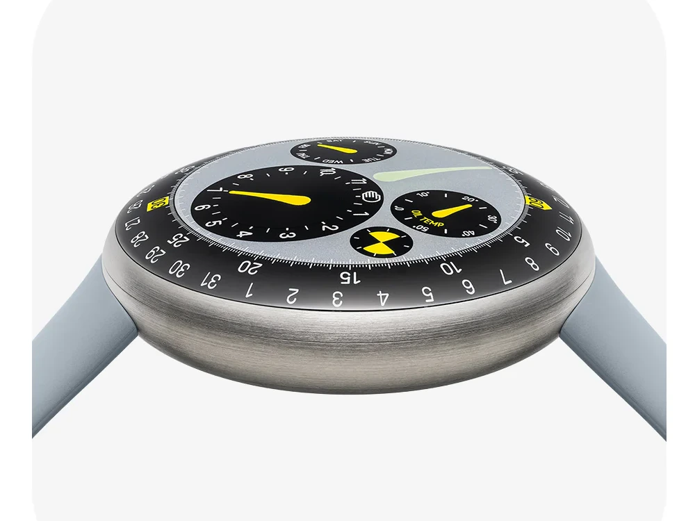 Marc Newson tasarımı Ressence Type 3 MN saati, fırçalanmış metal kasası, geleneksel ibreler yerine saati, günü ve tarihi gösteren dönen disklerle donatılmış karmaşık açık gri kadranı, parlak sarı vurguları ve açık gri kayışıyla beyaz bir zeminde dikkat çekici bir şekilde duruyor.