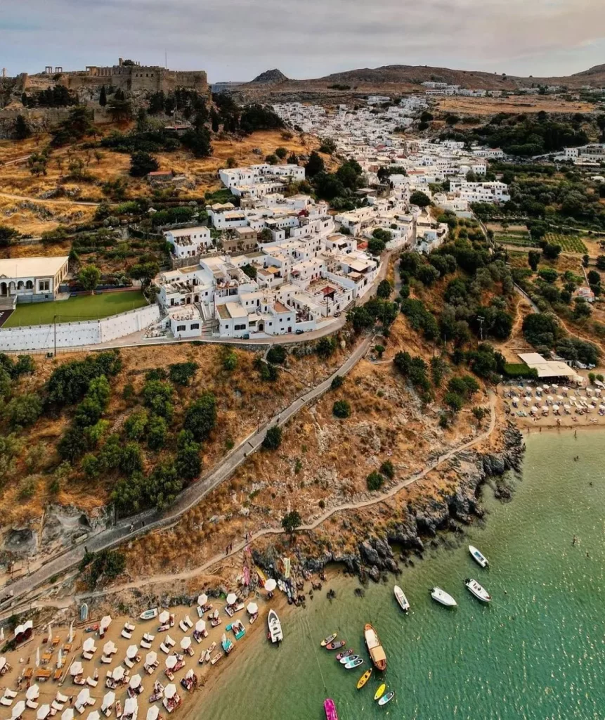 Rodos'un en popüler gezilecek yerlerinden Lindos'un kuşbakışı bu görüntüsünde, beyaz badanalı evlerin yamaçlara yayıldığı, tepede heybetli bir akropolün yükseldiği, berrak turkuaz sulara sahip iki kumsalında şemsiyelerin ve teknelerin görüldüğü, ziyaretçilerin keyifli anlar geçirdiği büyüleyici bir Akdeniz kasabası atmosferi belirginleşiyor.