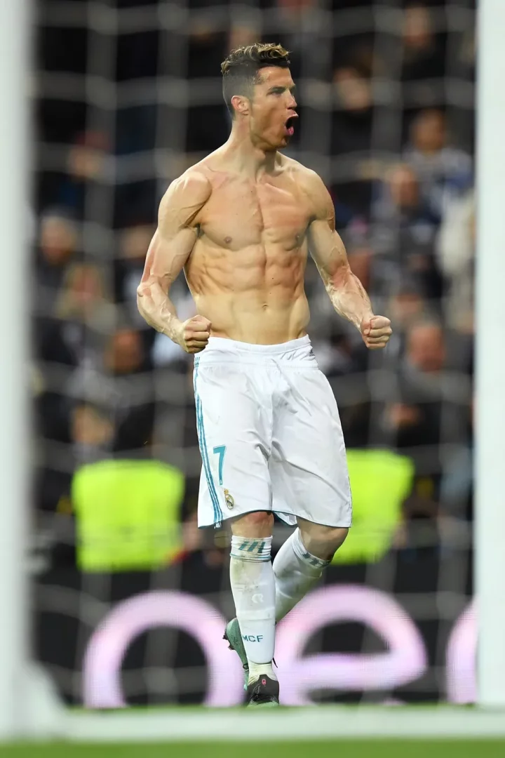 Futbol sahasında, filelerin önünde, beyaz şortuyla üstsüz duran ve ağzı açık şekilde kutlama yapan Cristiano Ronaldo, belirgin kasları ve formda vücuduyla dikkat çekiyor; bu görüntü, spor kariyerindeki olağanüstü fiziksel dayanıklılığının ve uzun ömürlülüğünün adeta bir kanıtı niteliğinde.