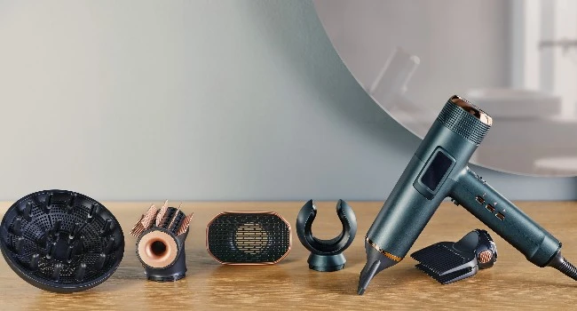 Rowenta Maestria saç kurutma makinesi, kıvırcık saçlar için difüzör, metalik detaylı şekillendirme, düzleştirme ve hacim verme gibi farklı fonksiyonlara sahip beş farklı başlığıyla ahşap bir yüzeyde modern bir sunumla sergileniyor.