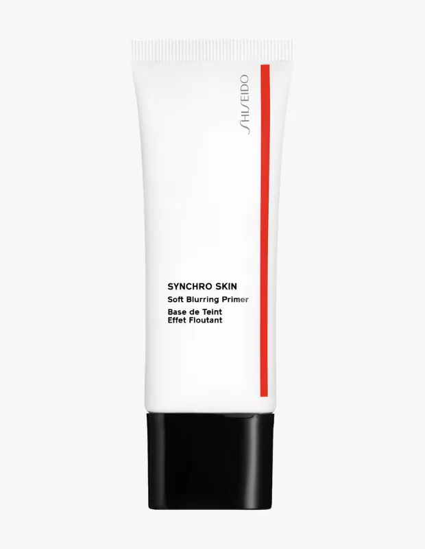 Beyaz bir arka plan üzerinde dikey duran, siyah kapaklı, sağında dikey kırmızı şerit ve Shiseido logosu bulunan SYNCHRO SKIN Soft Blurring Primer tüpü, ciltteki kusurları yumuşakça bulanıklaştıran bu makyaj bazının içeriğini gösteriyor.