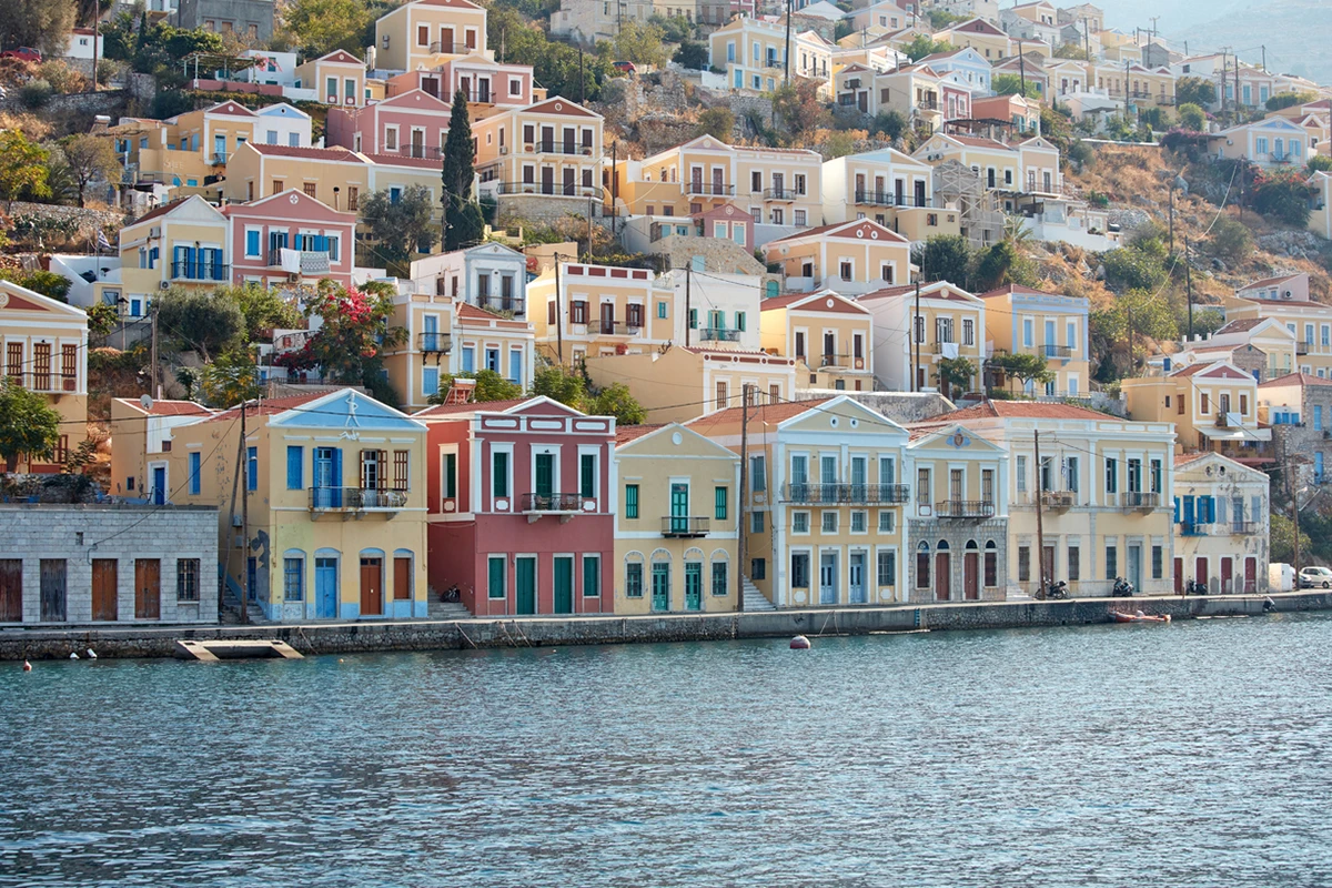 Simi Adası'nın meşhur Gialos Limanı'nda, Ege Denizi'nin parıldayan sularına sıralanmış, yamaca doğru yükselen pastel tonlardaki çok katlı neoklasik evler, adanın zarif ve kartpostal güzelliğindeki mimarisini gözler önüne seriyor.