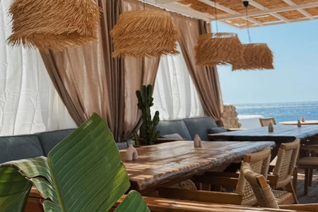 Spongia Hotel Süitleri'ndeki deniz manzaralı bu büyüleyici açık hava restoranı, doğal ahşap masalar, hasır avizeler ve yeşil bitkilerle süslenmiş, denizin huzur veren maviliğine karşı rahat bir yemek deneyimi sunan şık bir köşe.