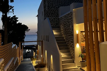 Alacakaranlıkta, denize doğru uzanan aydınlatılmış bir yol ve Spongia Otel'in taş duvarlı, beyaz yapısının modern basamakları, sıcak ışıklandırmalarla zarif bir akşam atmosferi sunuyor.