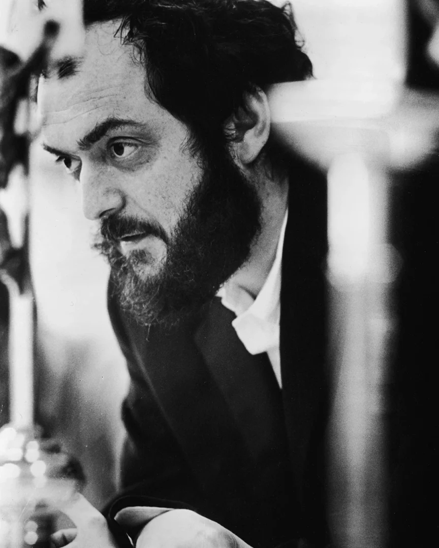 Belirsiz bir ekipmanla meşgul elleri ön planda, Stanley Kubrick'in gür sakallı, kıvırcık saçlı ve yoğun bakışlı yüzü, yaratım sürecine dalmış bir usta yönetmen olarak bu siyah beyaz karede dikkat çekiyor.