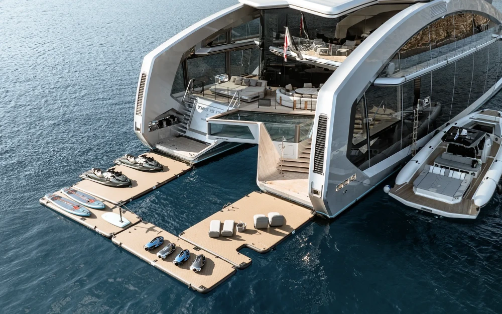 Tecnomar This Is It isimli modern motor katamaran süper yatın açık kıç güvertesinden denize uzanan yüzer platformlarda iki jet ski, dört e-foil ve iki sörf tahtası gibi çeşitli su oyuncakları sergilenirken, yatın lüks havuzu, dinlenme alanları ve yanında duran tender bot da bütüncül bir deniz yaşamı deneyimi sunuyor.