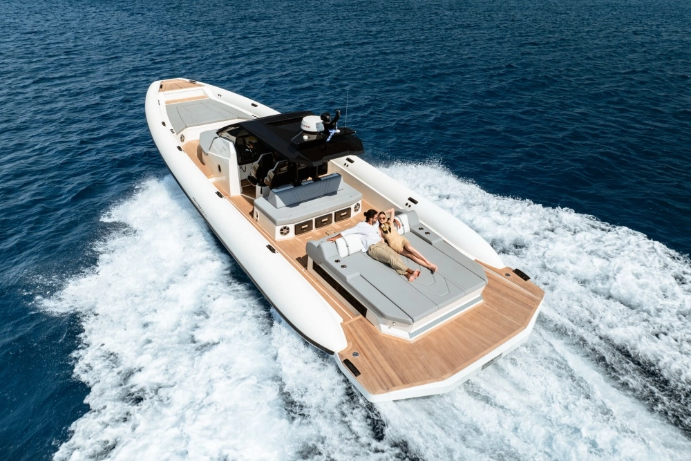 Açık mavi denizde hızla ilerleyen, arkasında köpüklü izler bırakan beyaz ve gri bir Technohull Chase Boat üzerinde, lüks bir süper yat deneyimi sunan geniş güneşlenme alanında uzanan keyifli bir çiftin kuşbakışı görüntüsü.