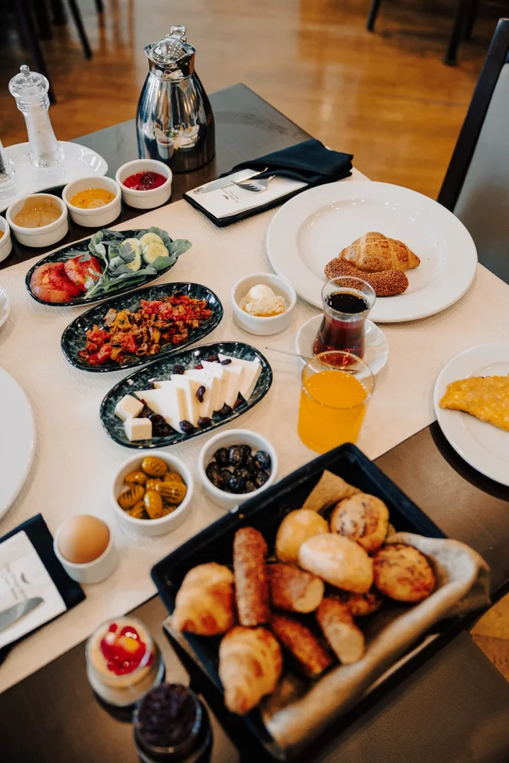 The Wings Hotels Ankara'nın zarif kahvaltı sofrasında simit, kruvasan, peynir çeşitleri, zeytinler ve taze sebzeler gibi özenle hazırlanmış birçok lezzet, butik lüks şehir oteli deneyiminin konforlu bir başlangıcını misafirlere sunuyor.