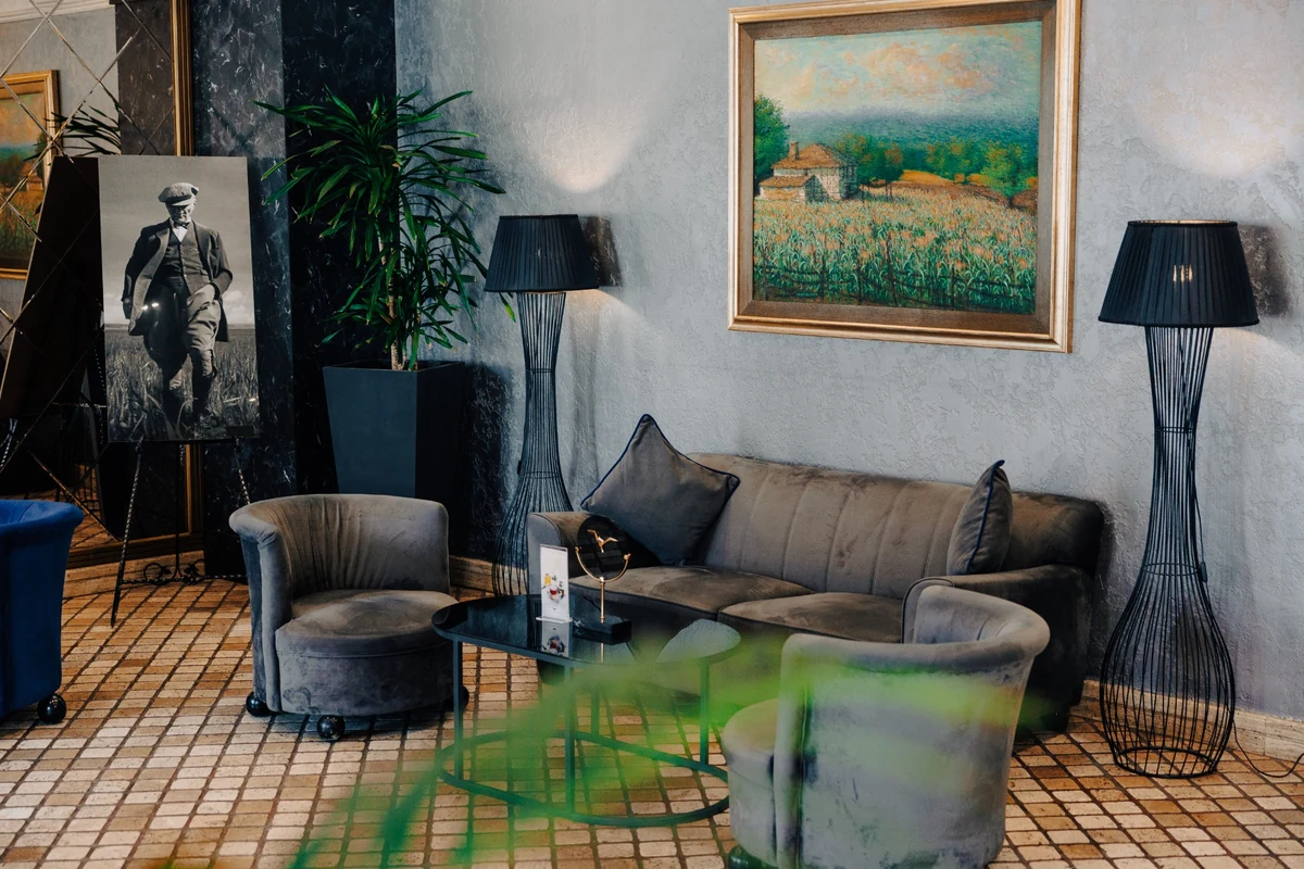The Wings Hotels Ankara'nın davetkar oturma alanı, gri kadife üçlü koltuk ve iki tekli berjerin çevresinde yer alan siyah oval sehpa, uzun metal ayaklı lambalar ve duvardaki geniş manzaralı tablo ile Atatürk portresiyle şık ve huzurlu bir dinlenme köşesi sunuyor.