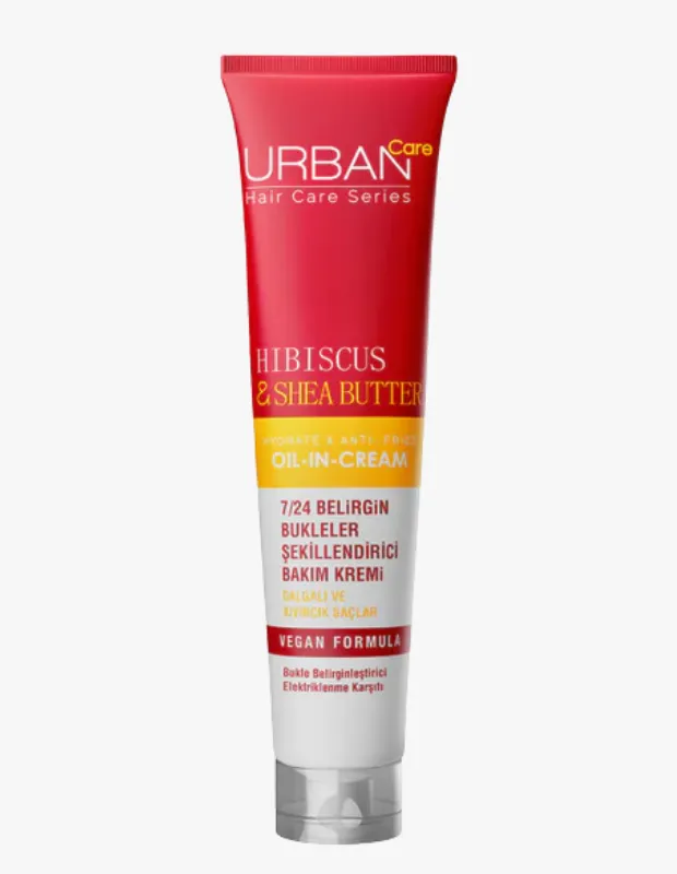 Beyaz bir arka plan üzerinde dikey olarak konumlanmış, kırmızı kapaklı ve üst kısmı kırmızı, alt kısmı beyaz renkteki Urban Care markalı Hibiscus & Shea Butter bukle belirginleştirici krem tüpü, dalgalı ve kıvırcık saçlar için 7/24 belirgin bukleler sağlayan vegan formülünü ön plana çıkarıyor.