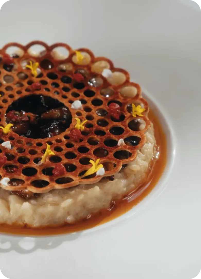 Vino Locale restoranında sunulan, kremalı pilav tabanının üzerinde koyu renkli sosu ve petek desenli, üzeri sarı çiçek yaprakları ile beyaz granüllerle süslenmiş çıtır wafelli, kenarlarında kahverengi sos bulunan zarif bir ana yemek tabağı.