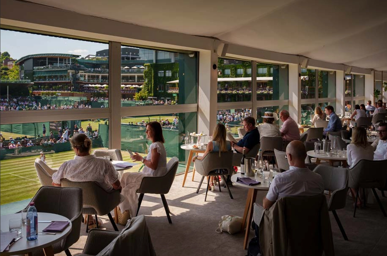 Wimbledon tenis turnuvasının kalbinde yer alan Centenary Restaurant'ta, şık giyimli konuklar, ikonik yeşil çim kortlara ve maçlara hakim geniş pencerelerin önünde oturarak, zarif bir öğle yemeği veya içki eşliğinde keyifli bir sohbet ve rafine bir gastronomik deneyim yaşıyorlar.