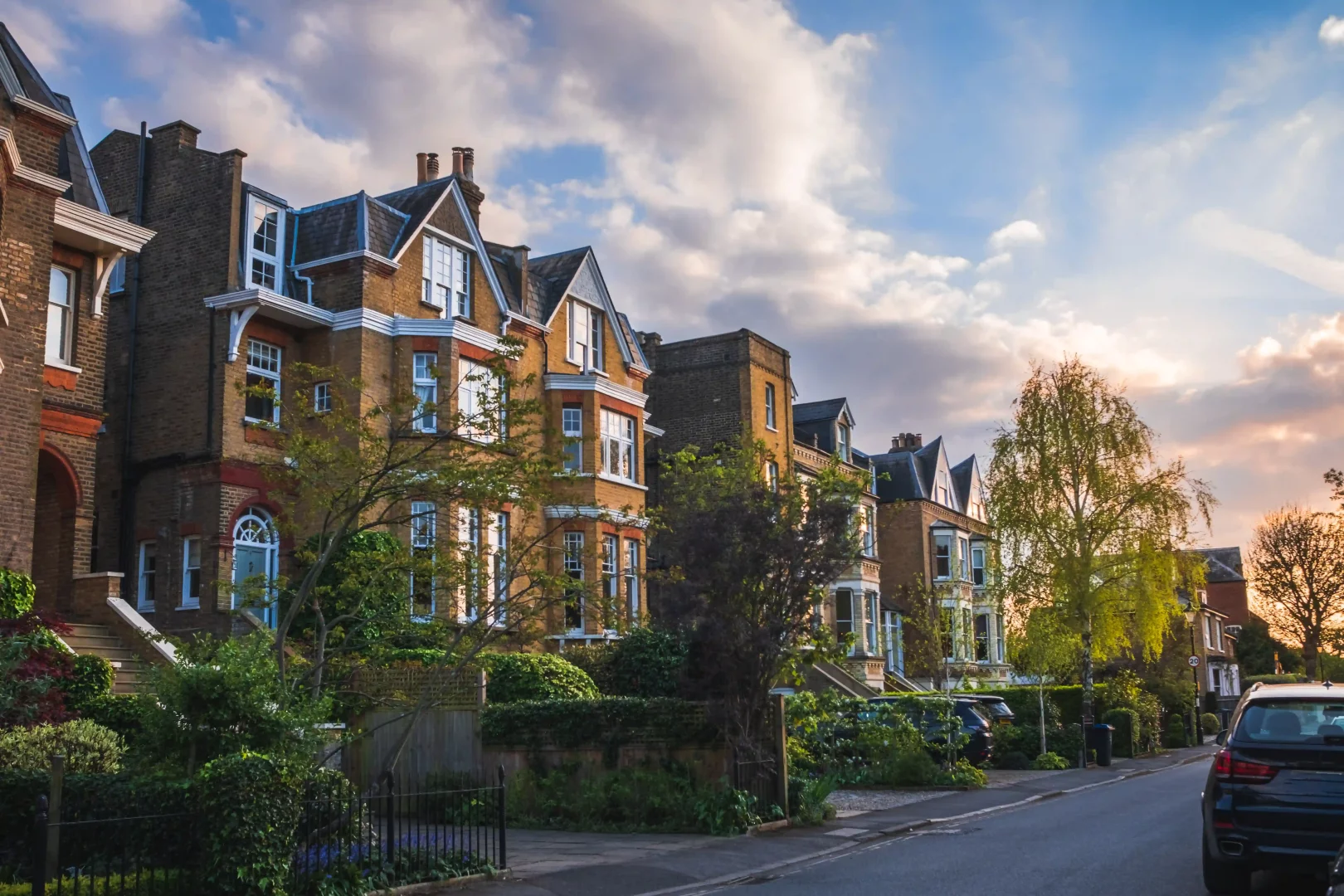 Wimbledon Village'ın Victoria döneminden kalma, yeşilliklerle çevrili ve gün batımının sıcak ışıklarıyla aydınlanan, zarif mimarili evlerin sıralandığı sakin bir sokağı, İngiliz yazının prestijli atmosferini yansıtıyor.