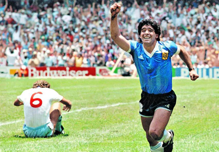 1986 Dünya Kupası çeyrek finalinde İngiltere'ye karşı Tanrı'nın Eli golünü attıktan sonra Arjantin formasıyla coşkuyla koşan Diego Maradona, yerde oturan 6 numaralı İngiliz oyuncunun arkasında kalabalık tribünler önünde zaferini kutluyor.