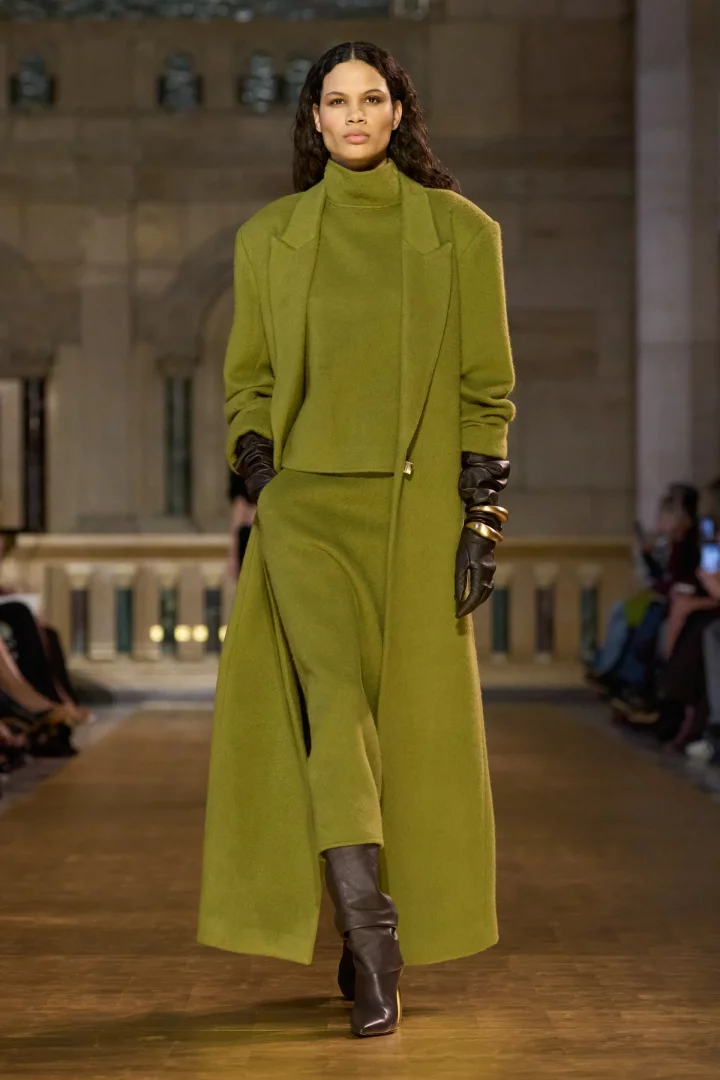 Podyumda yürüyen model, sonbahar renk trendlerinden Chartreuse (şartröz) renginde, uzun bir kaban, boğazlı kazak ve bol paça pantolondan oluşan monokrom bir Cult Gaia takımı, uzun deri eldivenler ve kahverengi botlarla sergileniyor.