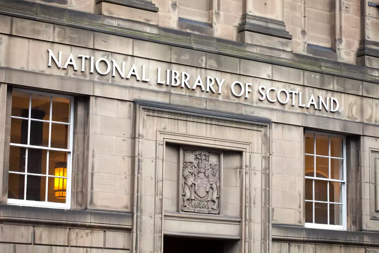 İskoçya Ulusal Kütüphanesi'nin görkemli taş cephesi, Edinburgh'un en güzel kütüphanelerinden biri olduğunu vurgularcasına büyük harflerle adını taşırken, iki yanında ışıltılı pencereler ve giriş üzerinde detaylı bir arma kabartması sergiliyor.