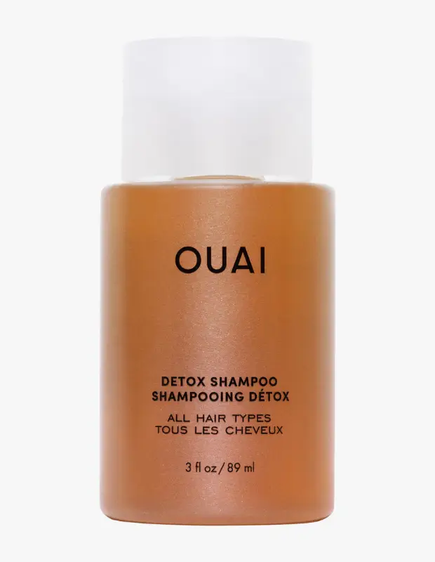 Beyaz arka plan üzerinde konumlanmış, beyaz kapaklı, parlak karamel rengi OUAI detoks şampuanı şişesi; ön yüzünde belirgin siyah harflerle DETOX SHAMPOO, ALL HAIR TYPES ve 89 ml / 3 fl oz bilgileriyle saç bakımı makalesi için ideal bir görsel sunuyor.