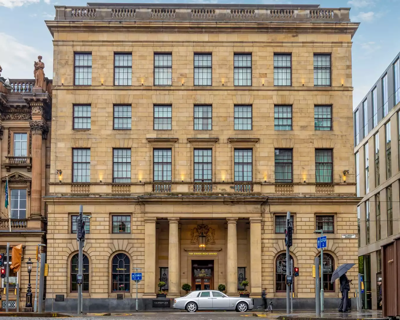 Ortasında belirgin sütunlu bir girişi ve üzerinde The Edinburgh Grand yazısı bulunan, kumtaşı renginde, geleneksel mimariye sahip, altı katlı gösterişli otel binası, önündeki ıslak caddede park etmiş parlak gümüş renkli lüks otomobille birlikte genel görünümünü sergiliyor.