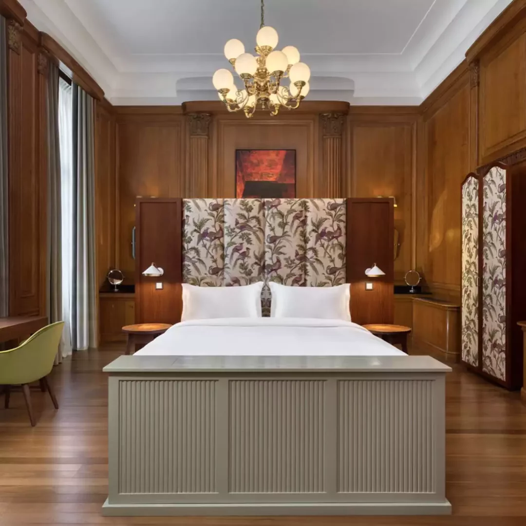 Edinburgh'un neoklasik mimarisini yansıtan zengin ahşap panellerle süslü bir otel süitinde, modern kuş desenli yatak başlığı ve tavandan sarkan gösterişli avize eşliğinde, şehirdeki büyük düşüncelere ilham veren çağdaş ve ihtişamlı bir konaklama deneyimi sunuluyor.