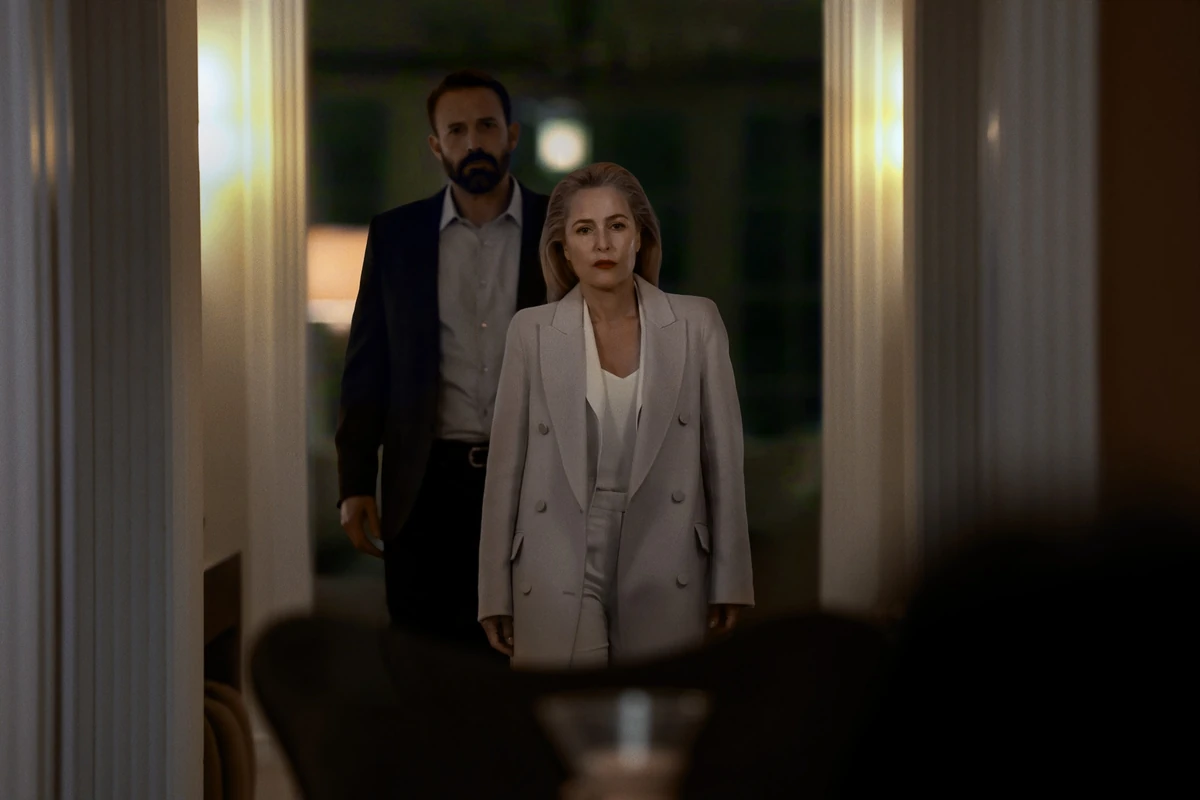 Netflix'in Animals filminin 2026'daki prömiyeri öncesi yayınlanan ilk karelerden birinde, açık gri kruvaze takım elbise giyen, ciddi yüz ifadesi ve kırmızı rujuyla öne çıkan sarışın bir kadın ile hemen arkasında duran sakallı, koyu renk takım elbiseli bir adam loş ışıklı bir koridor veya kapı aralığında ileriye bakıyor.