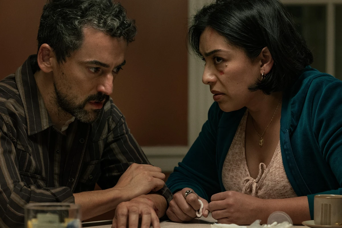Netflix'in Animals filminden bir ilk karede, yüzünde yara izi bulunan ve gergin görünen bir kadın ile ona endişeyle bakan bir erkek masada oturuyor; aralarında dağınık mendiller ve açık bir ilaç kutusu bu ciddi anı vurguluyor.