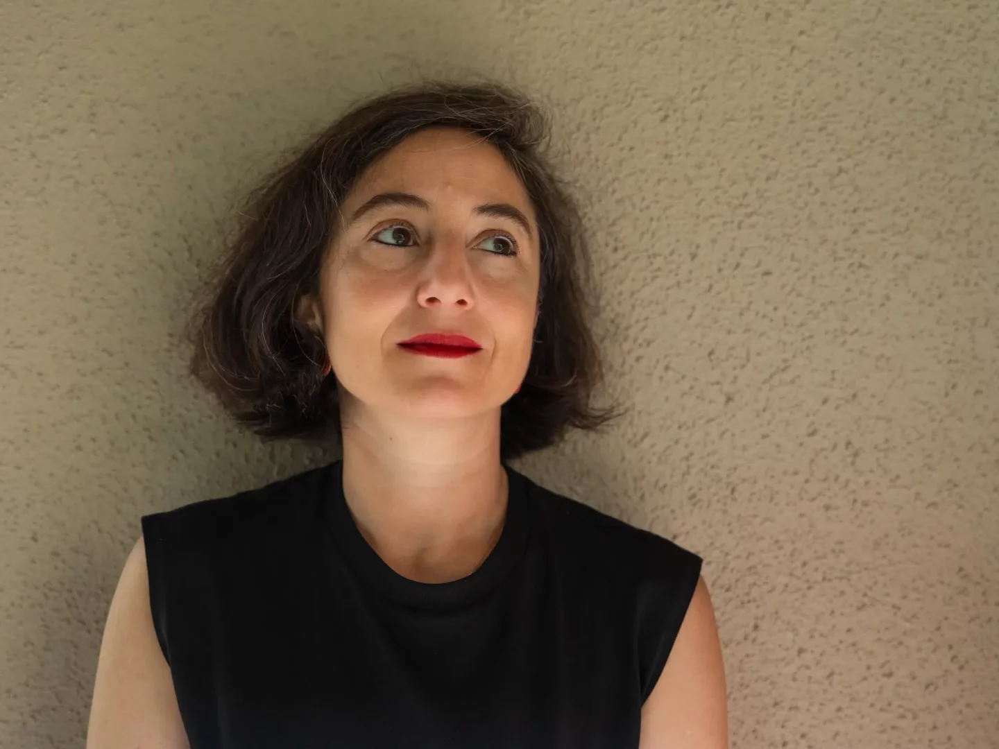 Ayşe Draz, müzede gerçekleşecek bir sahne etkinliği kapsamında çekilmiş yakın çekim portresinde, kısa kahverengi saçları, kırmızı ruju ve siyah bluzuyla, hafifçe yukarı doğru düşünceli bir ifadeyle bakıyor.