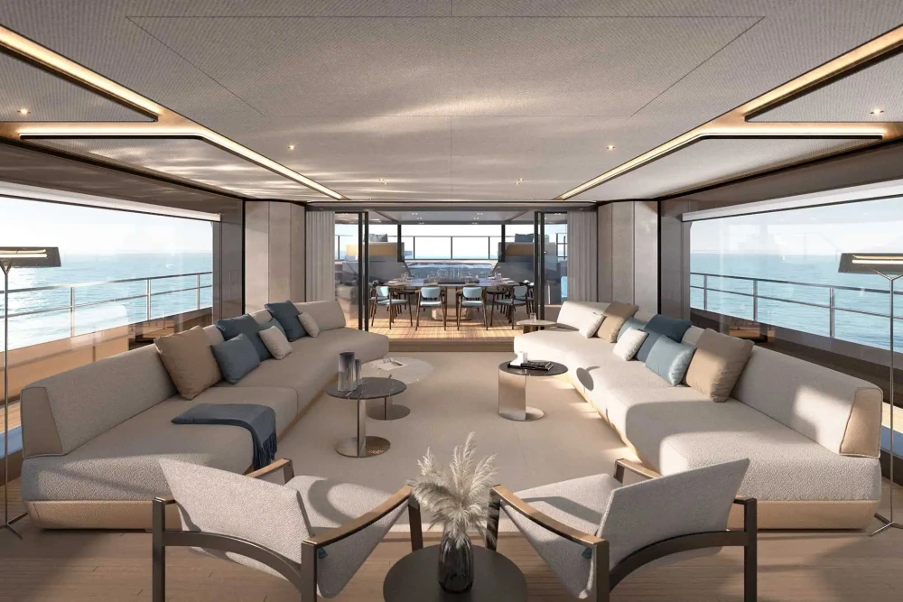 Bu Azimut Grande 44M süper yatın geniş salonunda, okyanus manzaralı pencerelerin önünde yer alan modern U şeklindeki bej kanepeler ve şık sehpalarla, ferah bir yaşam alanının konforu sergileniyor.