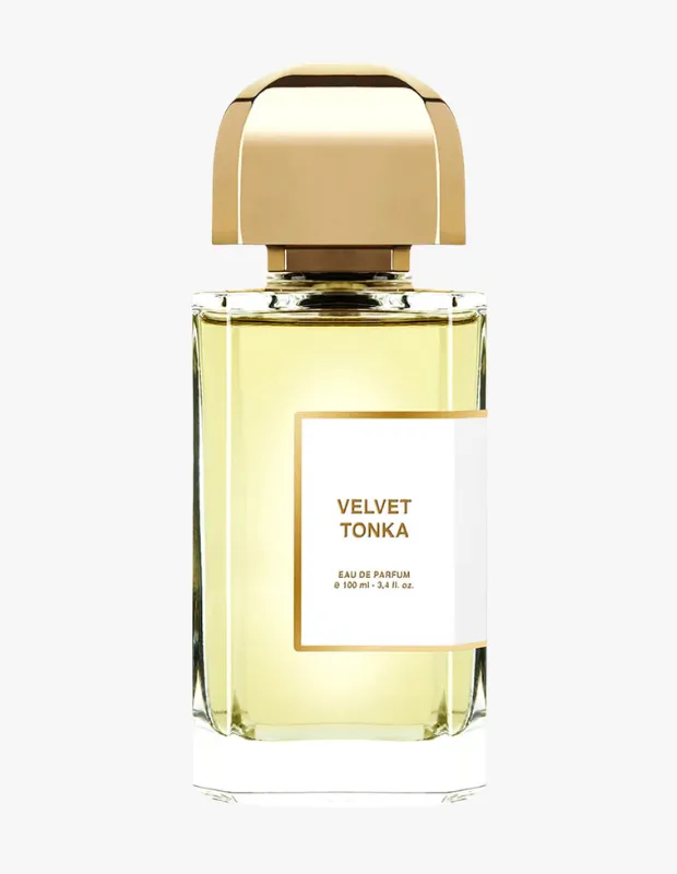 Aydınlık bir arka plan üzerinde duran, şeffaf, dikdörtgen cam şişedeki BDK Parfums Velvet Tonka EDP, parlak altın rengi kubbeli kapağı ve sarımsı içerikli sıvısıyla dikkat çekiyor, önündeki beyaz etikette Velvet Tonka Eau de Parfum e 100 ml yazısı okunaklı bir şekilde görünüyor.