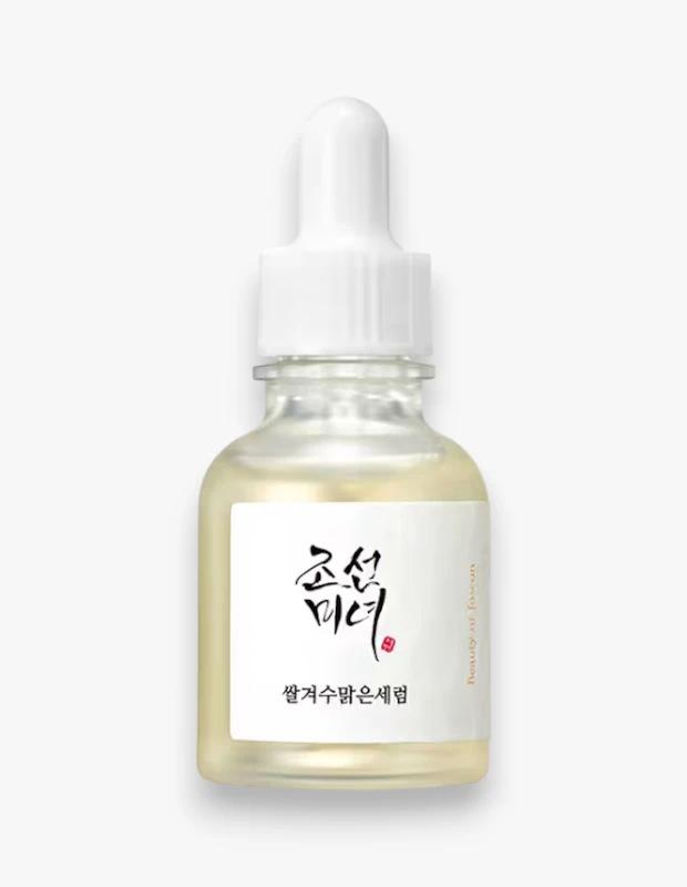 Beyaz bir arka plan üzerinde, ışığı yansıtan şeffaf cam şişedeki Beauty of Joseon Glow Deep Serum, beyaz damlalıklı kapağı ve içeriğindeki açık sarı parlatıcı derin serum ile net bir şekilde gösteriliyor.