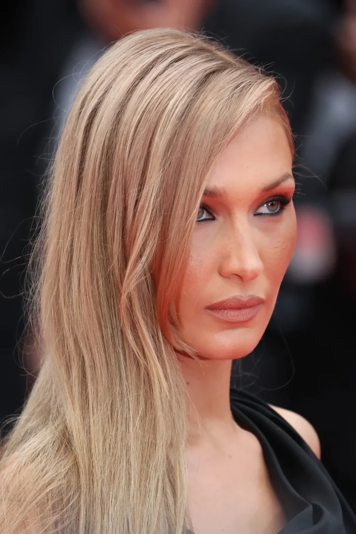 Bella Hadid'in açık kumral, uzun ve yandan ayrılmış saçlarının sol omzuna döküldüğü, kırmızı tonlarında göz makyajı ve doğal dudaklarıyla yukarı doğru baktığı bu yakın plan görüntü, modern perçem modellerine ilham veren zarif bir stil sunuyor.