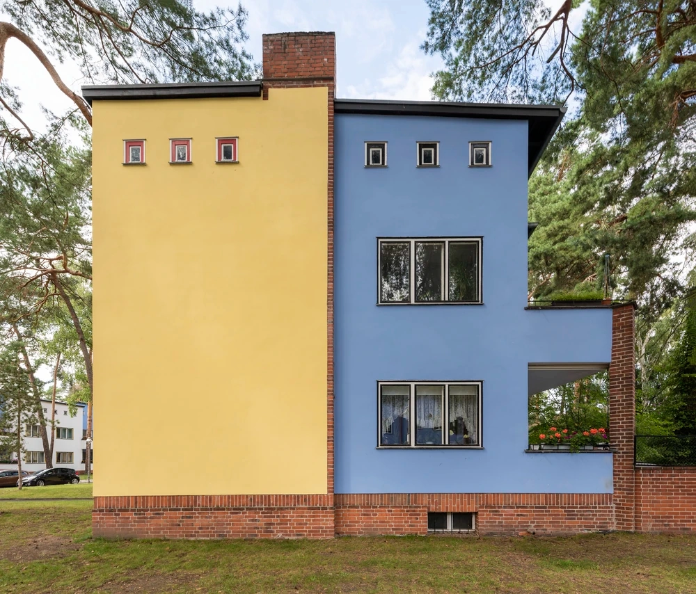 Ormanlık bir alanda konumlanan, özel renk prensiplerini yansıtan sarı ve mavi duvarları, düz çatısı ve heykelsi cephesiyle 20. yüzyıl modernist mimari ruhunu sergileyen bu Berlin Modernizm Toplu Konutları'ndan biri, 1926-1932 yılları arasında inşa edilen Waldsiedlung Zehlendorf'taki konut reformunun özgün bir örneğidir.