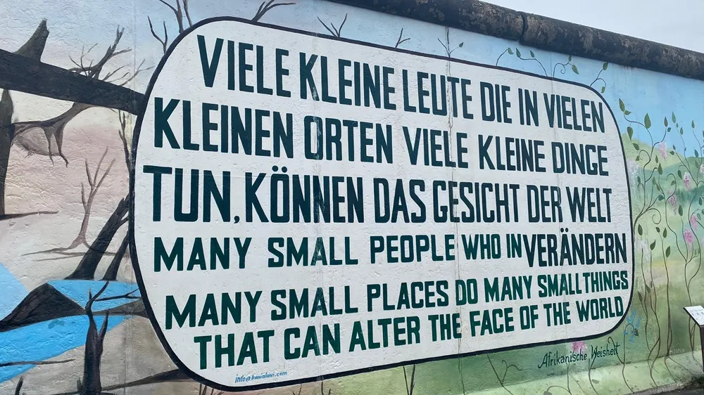 Berlin Duvarı'nın bir parçasını gösteren bu eserde, ortada büyük beyaz bir konuşma balonunda Almanca ve İngilizce olarak birçok küçük insanın birçok küçük yerde birçok küçük şey yaparak dünyanın çehresini değiştirebileceği mesajı yazılıyken, solunda kuru ağaçlar ve sağında yeşeren sarmaşıklarla pembe çiçekler görülüyor.