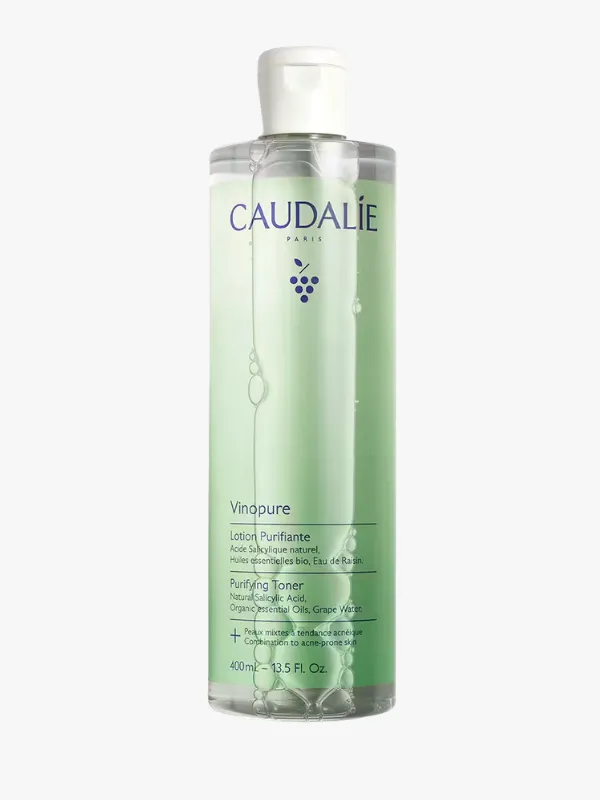 Caudalie Vinopure Purifying Toner'ın beyaz kapaklı, alt kısmı açık yeşil etiketli, içinde şeffaf sıvı bulunan 400 ml'lik şişesi, gözenek karşıtı arındırıcı tonik özelliği ile cilt bakımı için tasarlanmış olup üzerinde mor üzüm salkımı logosuyla net bir şekilde görülüyor.
