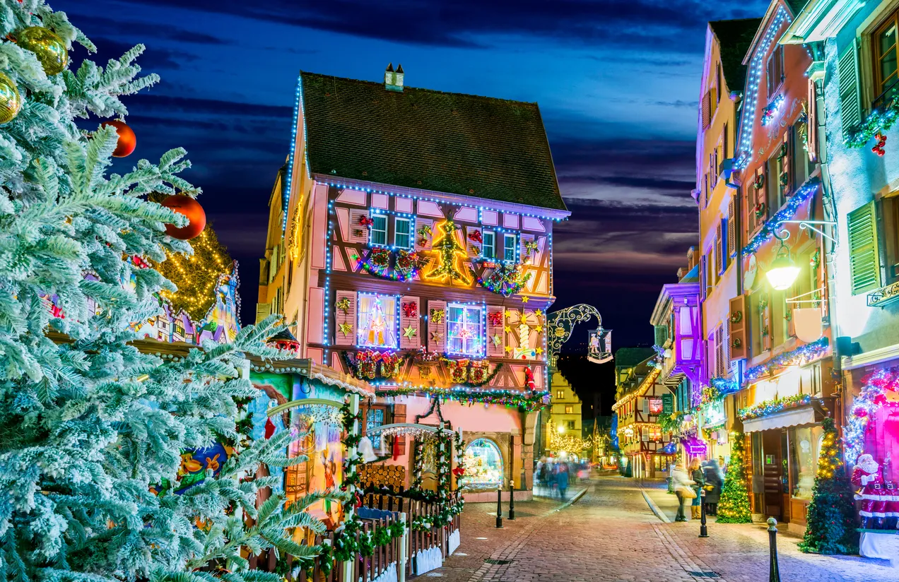 Gece vakti, Colmar'ın tarihi taş sokaklarında, Noel ruhunu yansıtan pastel tonlardaki yarı ahşap binalar ve karlı Noel ağacı ışıl ışıl rengarenk süslemelerle donatılmış, büyülü bir bayram atmosferi yaratıyor.