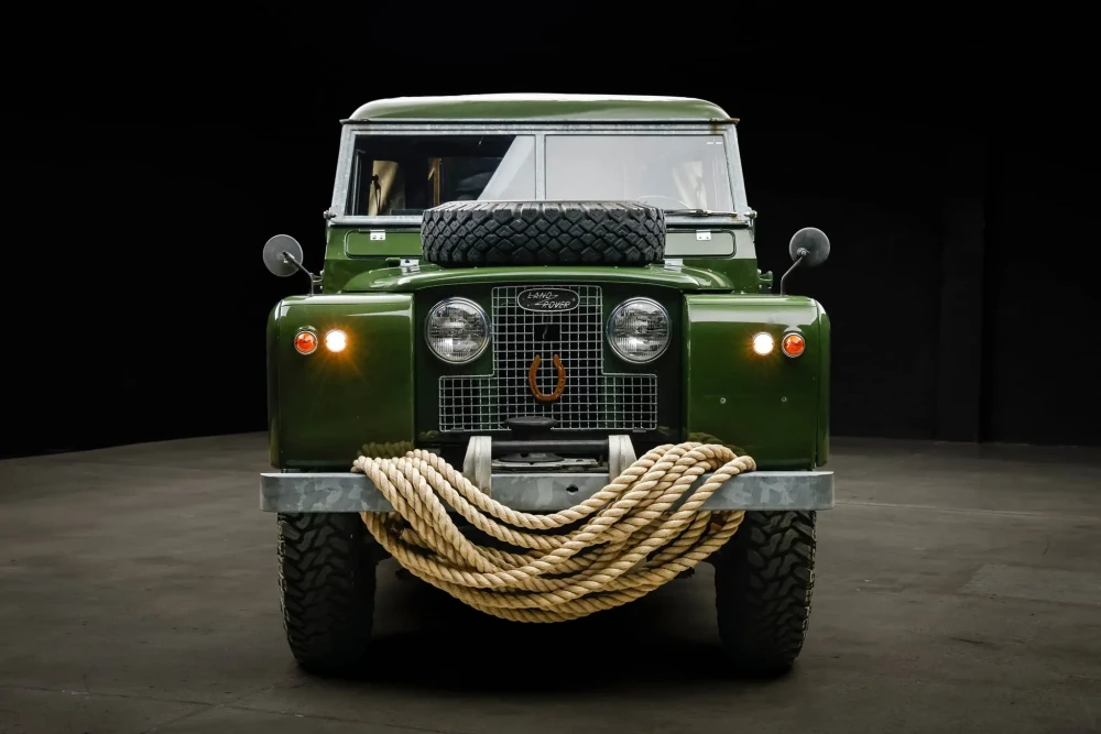 Farları açık, kaputunda yedek lastiği ve ön tamponunda kalın çekme halatı bulunan, Daniel Craig'e ait olduğu bilinen koyu yeşil klasik Land Rover Defender Series II modeli, açık artırma öncesi tüm detaylarıyla önden göz alıcı bir şekilde sergileniyor.