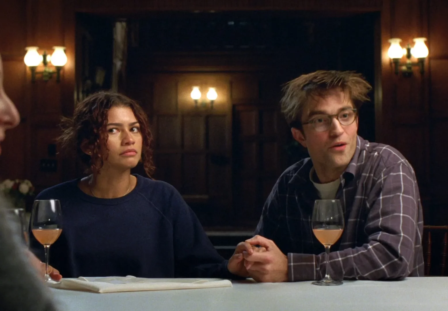 Zendaya'nın kıvırcık saçları ve koyu renkli kazağıyla, Robert Pattinson'ın da dağınık saçları, gözlükleri ve ekose gömleğiyle masada oturduğu, her ikisinin de ciddi ve meraklı bakışlarla bir drama veya sinema sahnesine odaklandığı bu an, izleyicilere yeni film önerileri sunuyor.