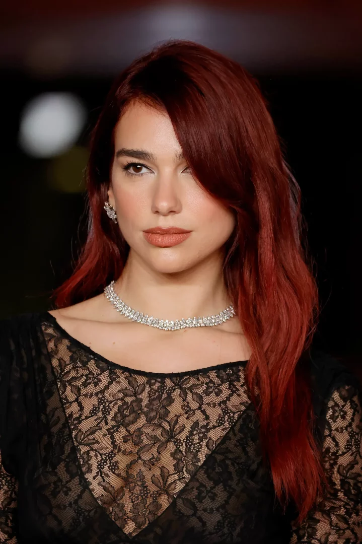 Dua Lipa, omuzlarına dökülen parlak kızıl dalgalı saçları, dikkat çekici elmas gerdanlığı ve siyah dantelli bluzuyla doğrudan kameraya bakarken, bakışlarıyla adeta esmerlere yakışan saç renkleri konusunda ilham veriyor gibi görünüyor.