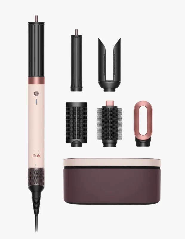 Açık pembe, siyah ve rose gold detaylara sahip Dyson Airwrap çoklu saç şekillendirici, ana ünitesi, farklı saç şekillendirme ihtiyaçlarına yönelik dalgalandırma, düzleştirme ve hacim verme başlıkları ile şık saklama kutusu beyaz bir zeminde görülebilir.