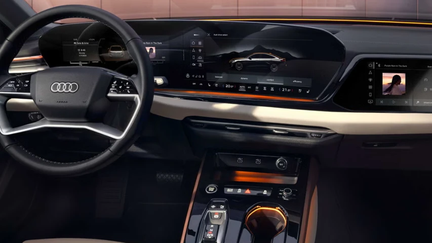 Bir premium otomobilin iç mekanından, Audi logolu direksiyonun ve geniş, kavisli dijital ekranların hakim olduğu modern kokpit; sürüş modları, multimedya kontrolleri ve zarif ambiyans aydınlatmalarıyla ileri teknoloji bir deneyim sunuyor.