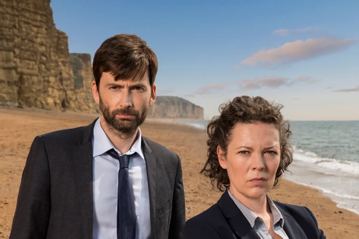 Broadchurch adlı popüler suç polisiye dizisinin dedektiflerini canlandıran David Tennant ve Olivia Colman, arkalarındaki heybetli kayalıklar ve denizin görüldüğü kumlu plajda ciddi yüz ifadeleriyle duruyor.