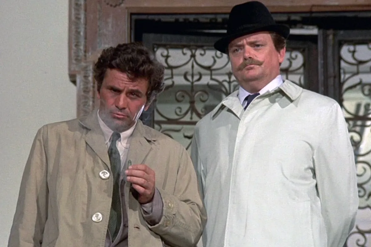 Columbo ile şapkalı ve bıyıklı bir karakter, trençkotlarıyla ciddi ifadeler takınarak yan yana duruyor; puro tutan Columbo’nun yer aldığı sahne, tüm zamanların en iyi suç ve polisiye dizileri arasındaki yapımın ikonik atmosferini yansıtıyor.