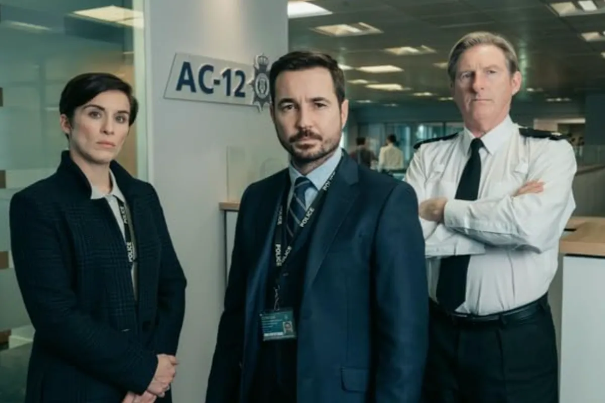 Line of Duty dizisinden, gergin bir atmosferde koyu ceketli bir kadın, lacivert takım elbiseli sakallı bir erkek ve üniformalı bir polis memuru AC-12 levhasının önünde duruyor; fotoğraf en iyi polisiye dizilerinin soruşturma atmosferini yansıtıyor.