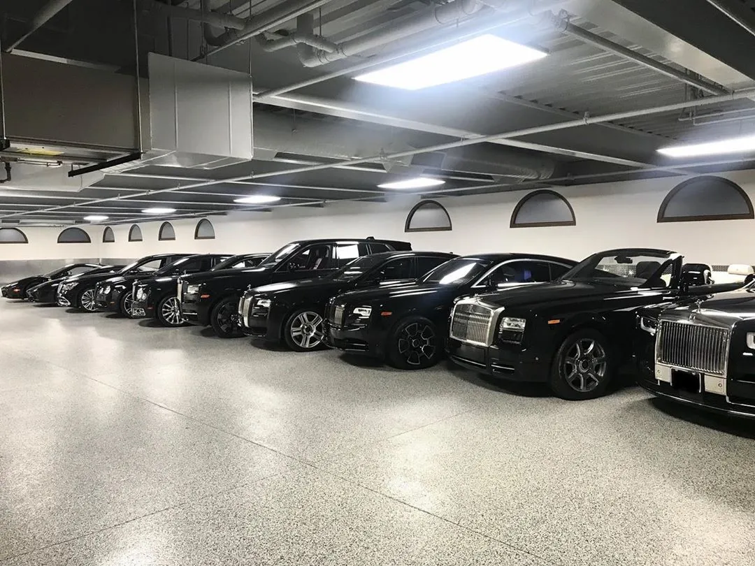 Floyd Mayweather'ın etkileyici lüks otomobil koleksiyonundan bir sahne; geniş ve iyi aydınlatılmış bir garajda yan yana park edilmiş, parlak siyah renkte birçok Rolls-Royce modelinin ve diğer lüks araçların sergilendiği görkemli bir görüntü.
