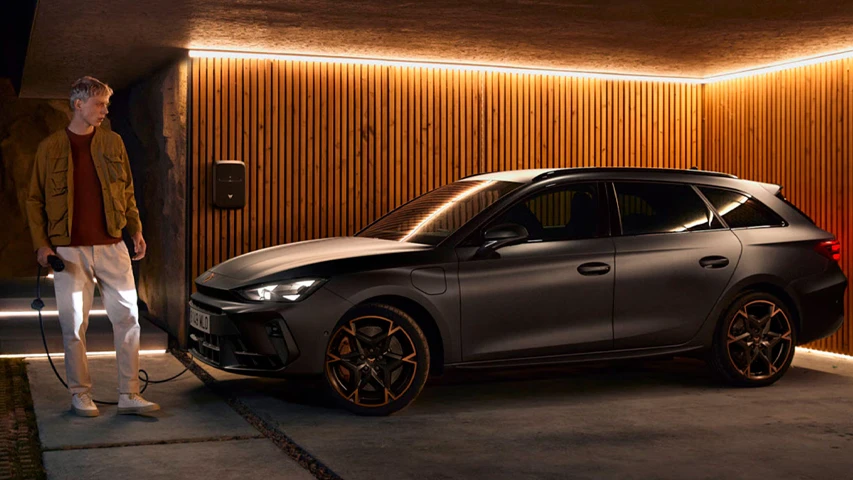 Modern ahşap panelli bir garajda, bir genç adam koyu mat renkli, sportif bir plug-in hybrid station wagon arabayı şarj istasyonuna bağlarken, bu tip hybrid araçların sunduğu yakıt verimliliği ve çevre dostu birçok avantaj belirginleşiyor.