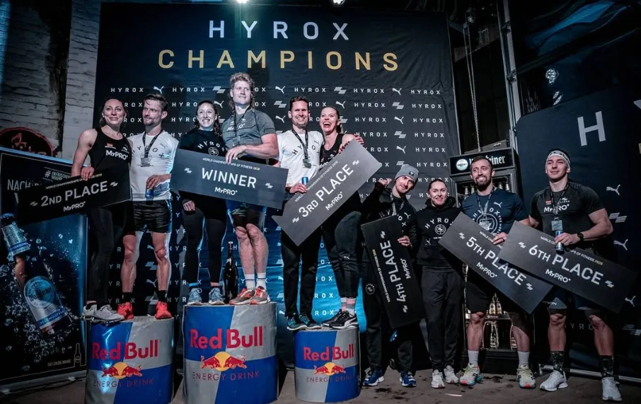 Hyrox Dünya Fitness Şampiyonası 2020'nin ardından Red Bull varillerinden oluşan şampiyonluk podyumunda coşkuyla duran, birinci, ikinci, üçüncü, dördüncü, beşinci ve altıncı sırayı gösteren pankartlar tutan dokuz sporcu, bu global fitness yarış formatının sunduğu yeni meydan okuma ruhunu yansıtıyor.
