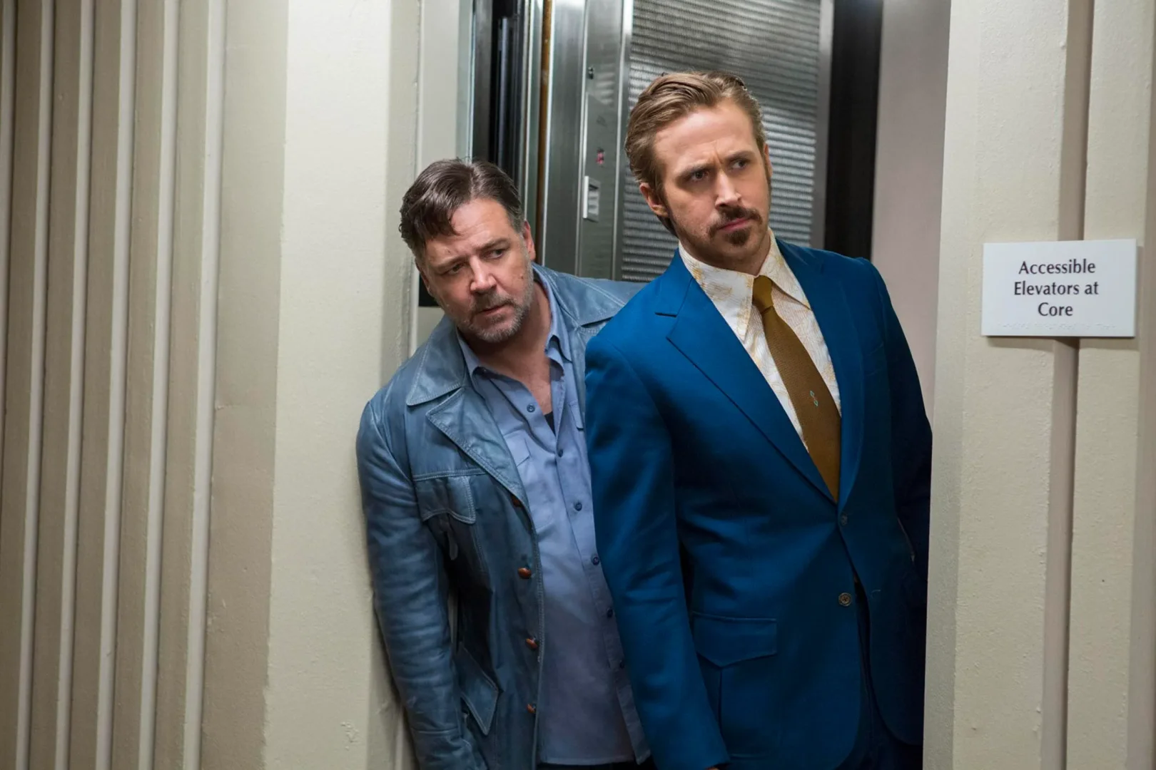 İyi Adamlar filminden alınmış bu karede, parlak mavi takım elbisesi ve altın rengi kravatıyla Ryan Gosling ile açık mavi deri ceketiyle Russell Crowe, endişeli bakışlarla bir koridorda köşeden bakarak sinema eleştirmeni tarafından seçilen filmleri temsil ediyor.