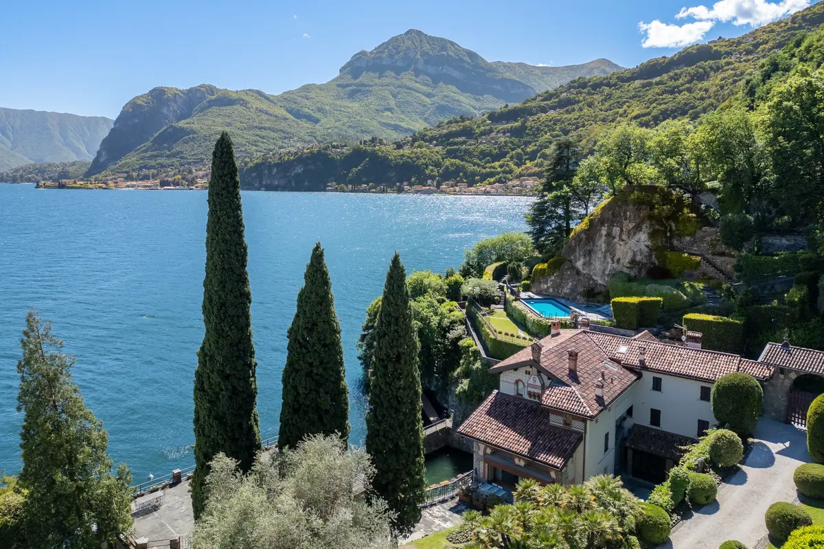 Güneşli bir havada Como Gölü'nün masmavi sularına bakan, yemyeşil selvi ağaçları, teras bahçeler ve yamaçtaki kayalık bir alana inşa edilmiş James Bond Villa La Gaeta'nın kiremit çatılı ana yapısı ile parıldayan mavi havuzunu gösteren büyüleyici manzara.