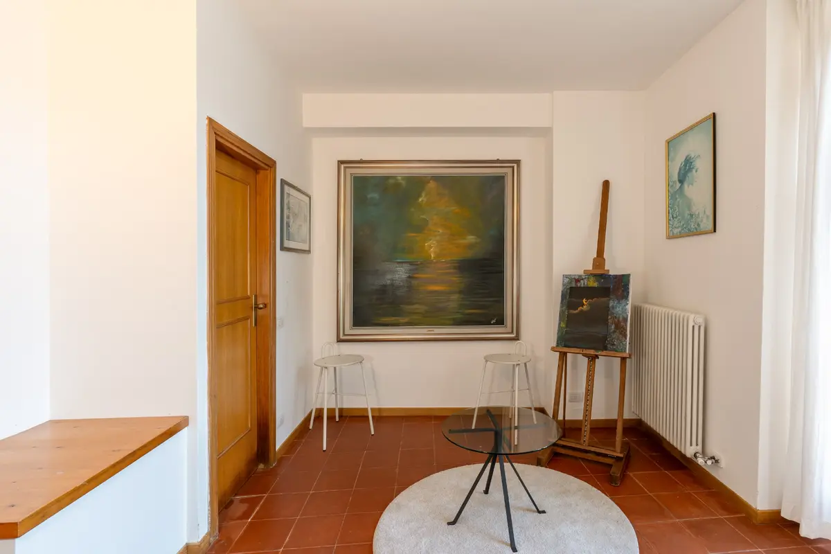 James Bond Villa La Gaeta'nın huzurlu sanat köşesinde, terakota karolu zemin üzerinde, parıldayan gün batımını yansıtan büyük bir tablo duvarı süslerken, bir şövale üzerinde duran başka bir eser ve küçük bir cam sehpa ile çevrili minimalist tabureler sanatsal bir atmosfer yaratıyor.