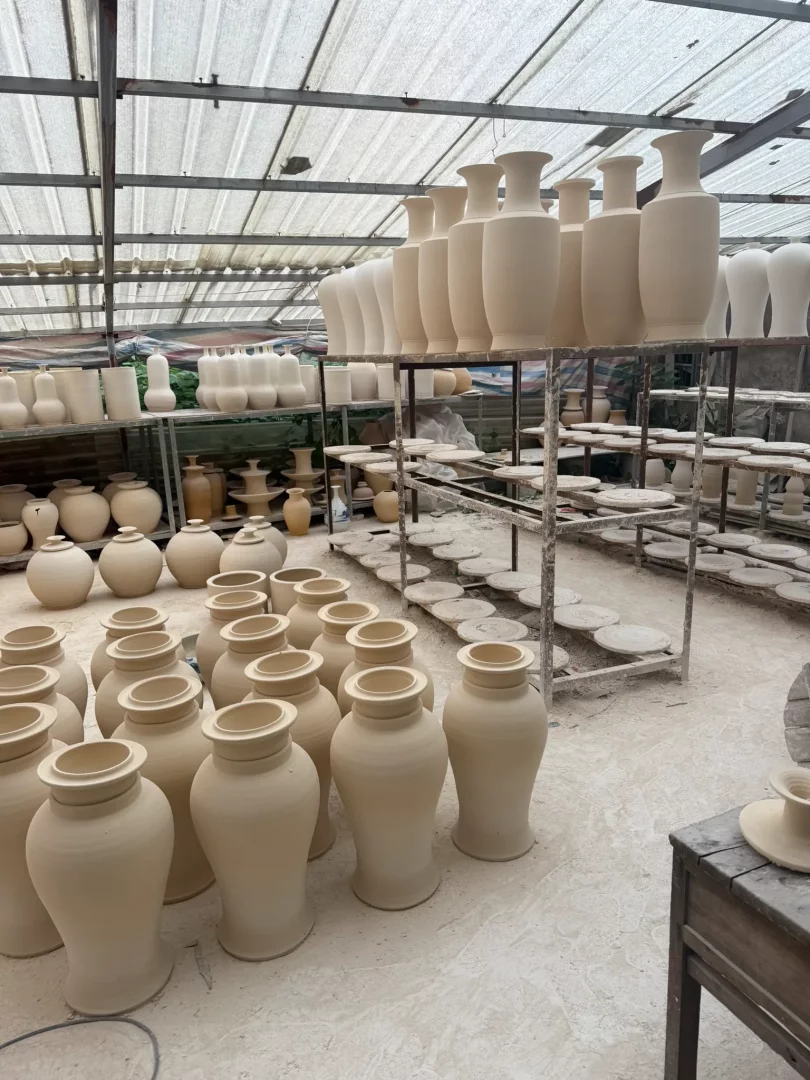 Jingdezhen'in Porselen Başkenti kimliğini yansıtan bir atölyede, raflarda ve zeminde kurutulmaya bırakılmış, henüz sırlanmamış yüzlerce farklı boyutta geleneksel porselen vazo ve çeşitli formdaki seramik ürünleri, şehrin kesintisiz üretim kültürünü gösteriyor.