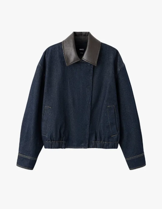 Stüdyo çekiminde beyaz arka plan önünde sergilenen, derin koyu mavi denim kumaştan üretilmiş, geniş kahverengi suni deri yakası, bol kesimi ve lastik manşetleriyle modern bir stil sunan bomber kot ceket.